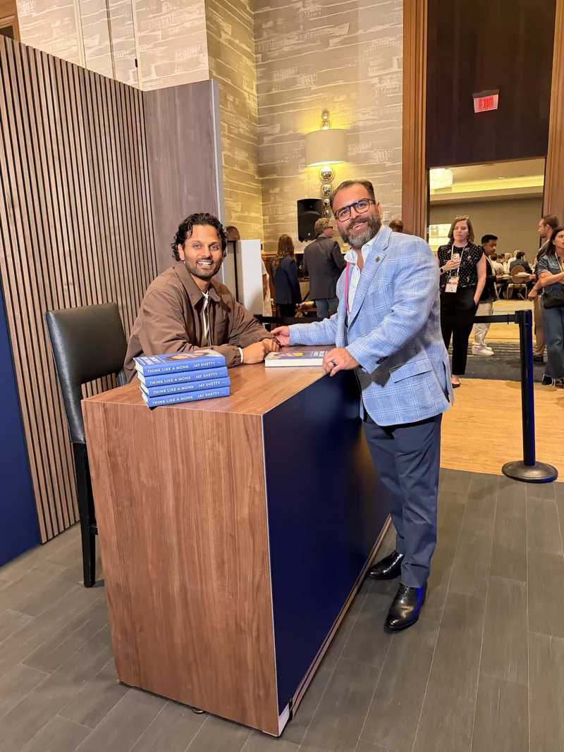 Steven standing beside Jay Shetty at a book signing table stacked with copies of Think Like a Monk