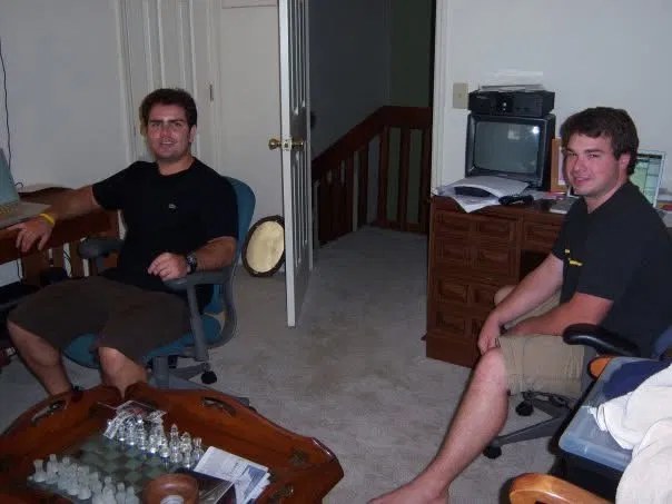 Two recent graduates in a spare bedroom with a laptop and business cards on a chess table, SpartX in 2006