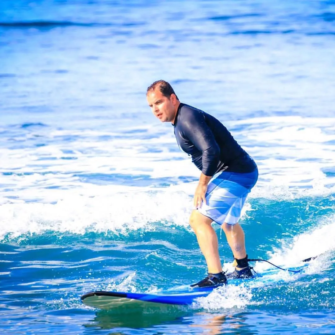 Steven Gonzalez riding a small wave on a soft-top surfboard, knees bent, arms out