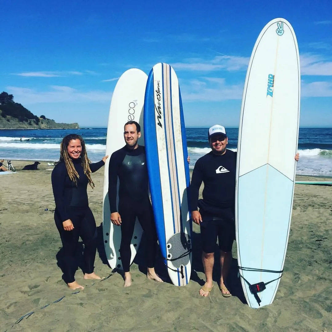 Three surfers standing on a beach with soft-top surfboards